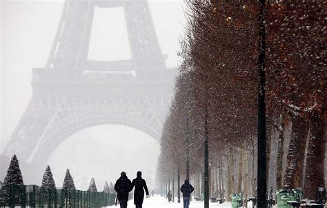 A Clock Tower In The Middle Of A Snowy Street With People Walking On It And Trees